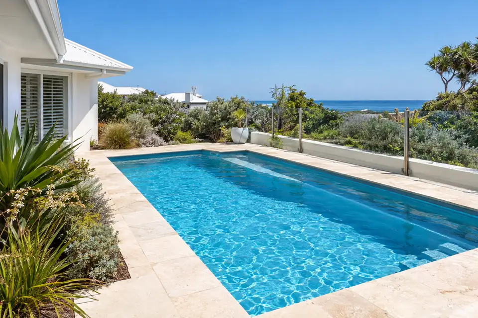 Backyard pool beside a white rendered home with the ocean in view