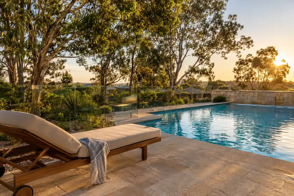 Sun lounge and towel beside a clear backyard pool at sunset