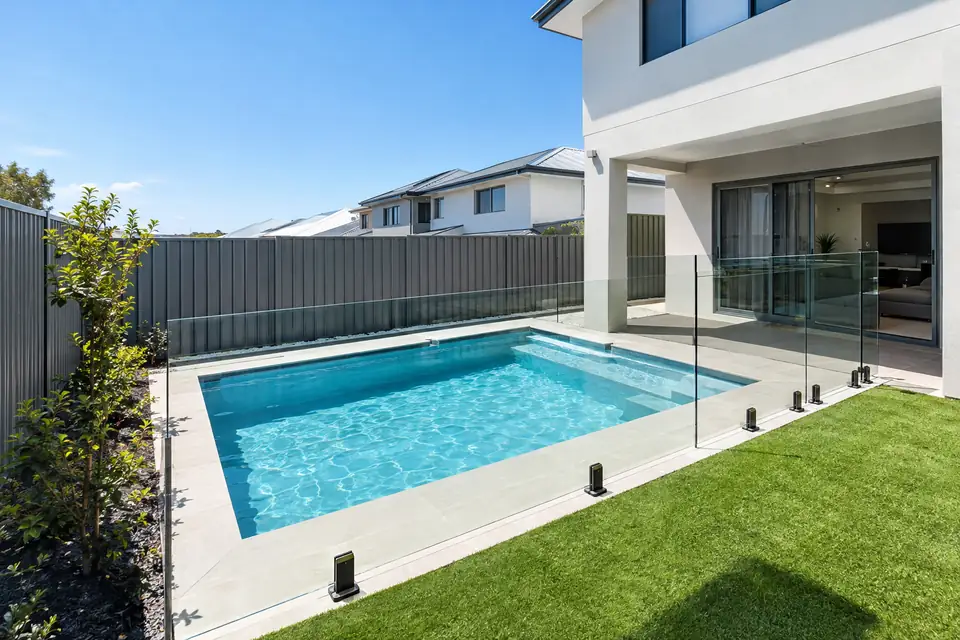 Compact plunge pool with a glass fence beside a newer double-storey home